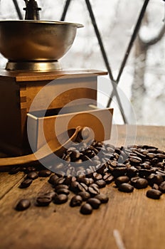 Old antique coffee grinder with coffee beans on a wooden windowsill.