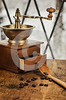 Old antique coffee grinder with coffee beans on a wooden windowsill.