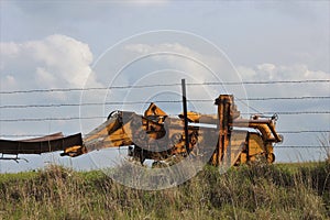 Old Antique Combine in a farm pasture with blue sky and a fence out in the country in Kansas.