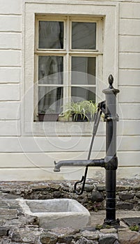 Old antique hand operated water pump in front of the wall.