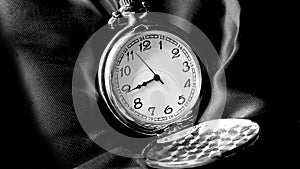 Old antique pocket watch showing time on black material. Black and white photography