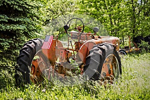 Old Antique Tractor with a United States Flag in an Overgrown Field
