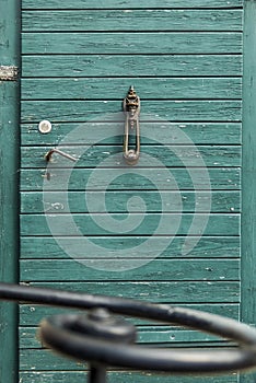 Old, antique wooden door with nostalgic door knocker with rogue motive in the foreground a wrought iron handrail