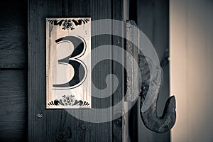 Old apartment number sign on the wall of wood with the number three on it