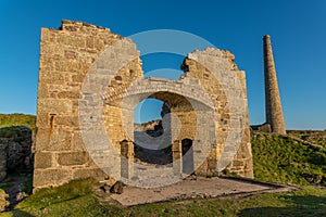 The old arched wall of Brunton calciner, with tin mine chimney, at Botallack, Cornwall