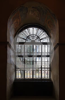 Old arched window in a church with iron grilles in front