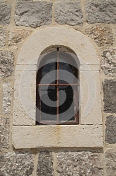 Old arched window with metal grill on stone facade in Montenegro