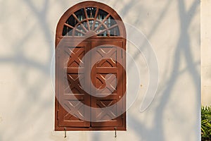 Old arched wooden window on white wall with shadows of tree bran