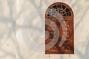 Old arched wooden window on white wall with shadows of tree bran