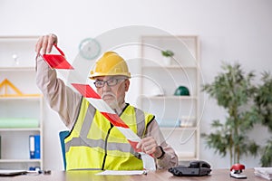 Old male architect holding caution tape