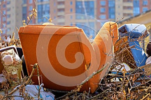 An old armchair on the garbage heap of the city dump in the background of residential building. Household unsorted