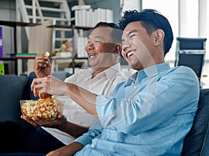 Old  Asian father was spending joyful time with mature adult son at home  on couch