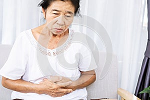 Old Asian female suffering from stomach ache hand holding her abdominal pain