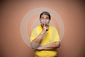 old asian man with be quiet or shush gesture in plain background