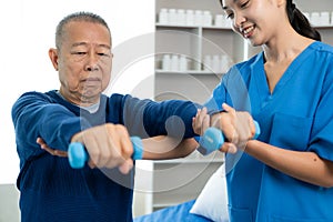 An old Asian man is doing physical therapy with the support of a nurse in the living room by exercising