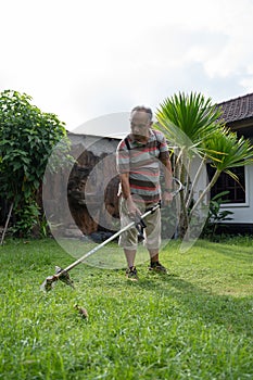 Old asian man mowing his garden