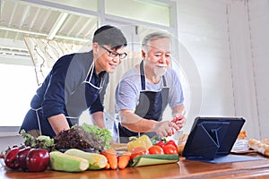 Old Asian man in retirement age spending time to learning how to cook healthy food from internet with his son with vegetables