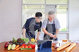Old Asian man in retirement age spending time to learning how to cook healthy food from internet with his son with vegetables