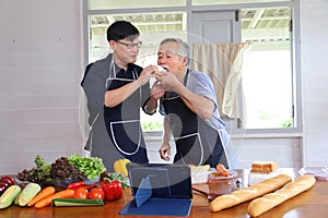 Old Asian man in retirement age spending time to learning how to cook healthy food from internet with his son via digital tablet