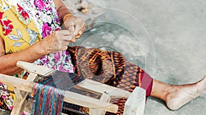 An Old asian women hold silk of thread near rool of silk onthe ground