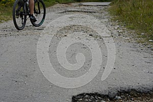 Old asphalt road with many potholes and the cyclist which is trying to avoid the obstacles.