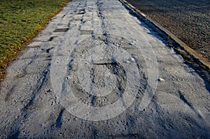 The old asphalt surface covers the old paving which was painted in the morning sun. the crooked and cracked sidewalk surface, froz