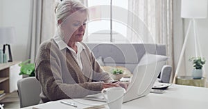 Old Author writing a book on a laptop sipping some tea or coffee at home. A senior female writer typing her life story