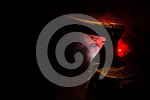 Old ax attached to the tree trunk on horror red foggy background. Scary Halloween theme with maniac killer weapon