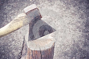 The old ax is stuck in an old log on the background of the ground.