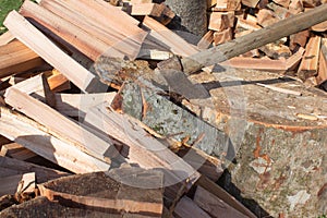 Old axe standing against a piled pieces of firewood. Axe stuck in a stump