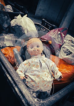 an old baby doll in a dumpster. social concept. Unwanted children, orphans