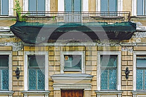 An old balcony in disrepair covered with a green professional construction protective net. Facade of a residential building in St.