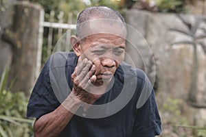 An old balding asian man suffering from an aching molar. Attempting to relieve the pain. Experiencing a bad toothache or dry