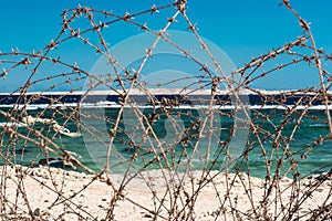 Old barbed wire infront of sea. Wire and blue sky with clouds. Safety fence of barbed wire against the blue sky and sea