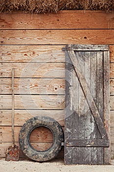 Old barn door, dirty old tire and shovel leaning against the wooden barn door