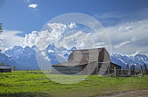 Old barn in a field under the Grand Teton mountains with dramatic clouds