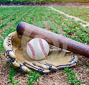 Old baseball, glove, and bat on field with base and outfield in background