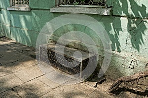 Old basement window with black dirty iron bars on the green concrete wall of the building