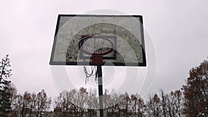 Old basketball hoop on grunge destroyed schoolyard. Gray rainy sky sad town mood. Metal chain basket on hoop. Outdoors