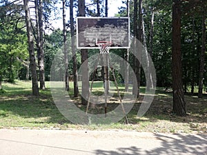 Old basketball hoop in a village court with forest in background
