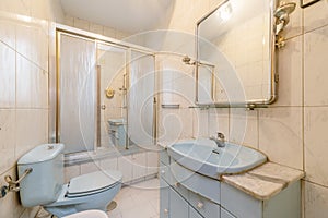 Old bathroom with blue toilets, mirror on the wall, shower cabin with screens and the rest of the house in the same condition