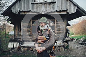 Old bearded forester posing in front of old wooden hut