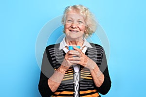 Old beautiful smiling woman holding a cup of tea and looking at the camera