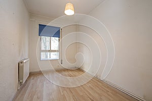 Old bedroom with a small aluminum window with a blue shutter, walls in need of a coat of paint and laminated flooring