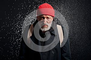 Old beggar man in street clothes stand under rain