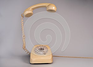 Old beige aged rotary telephone with removed hanging receiver on grey background. Vintage landline home phone with dial