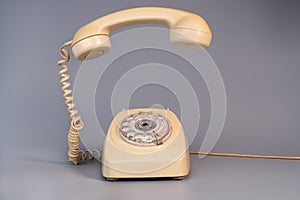 Old beige aged rotary telephone with removed hanging receiver on grey background. Vintage landline home phone with dial