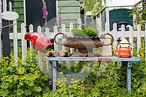 Old bench with pots, watering can and flowers in the backyard. Cozy village garden with plants, bench and white fence.