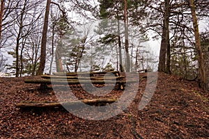 Old bench from tree in forest and fallen leaves on ground and wood sculpture in background, Slovakia Sulovske Vrchy