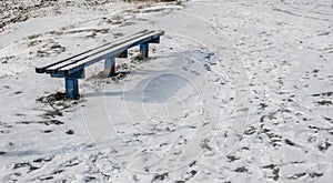 An old bench on white snow field and  icy footprints